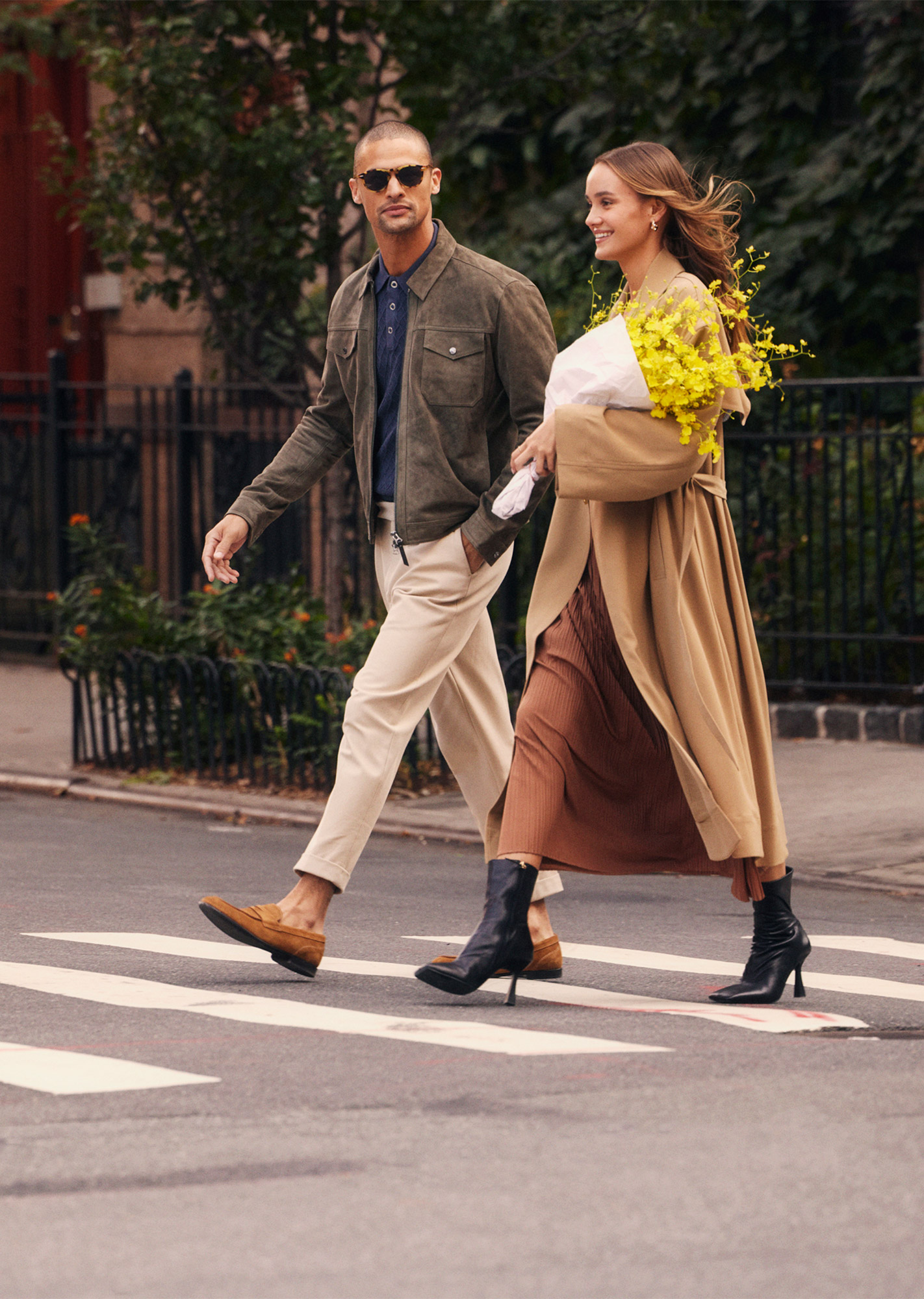 Man wearing glasses and woman holding yellow flowers walking down the street